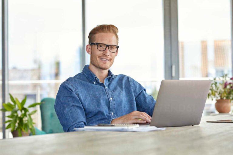 Portrait of smiling young man sitting at table using laptop